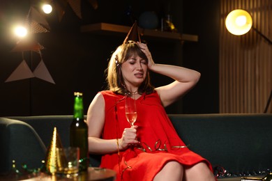 Photo of Woman with glass of alcohol suffering from hangover on sofa in messy room after party
