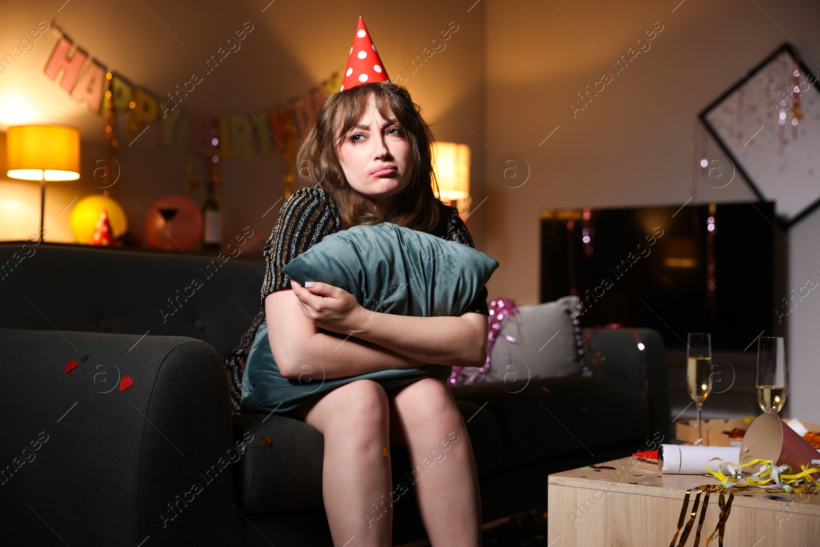 Photo of Woman with pillow suffering from hangover on sofa in messy room after party