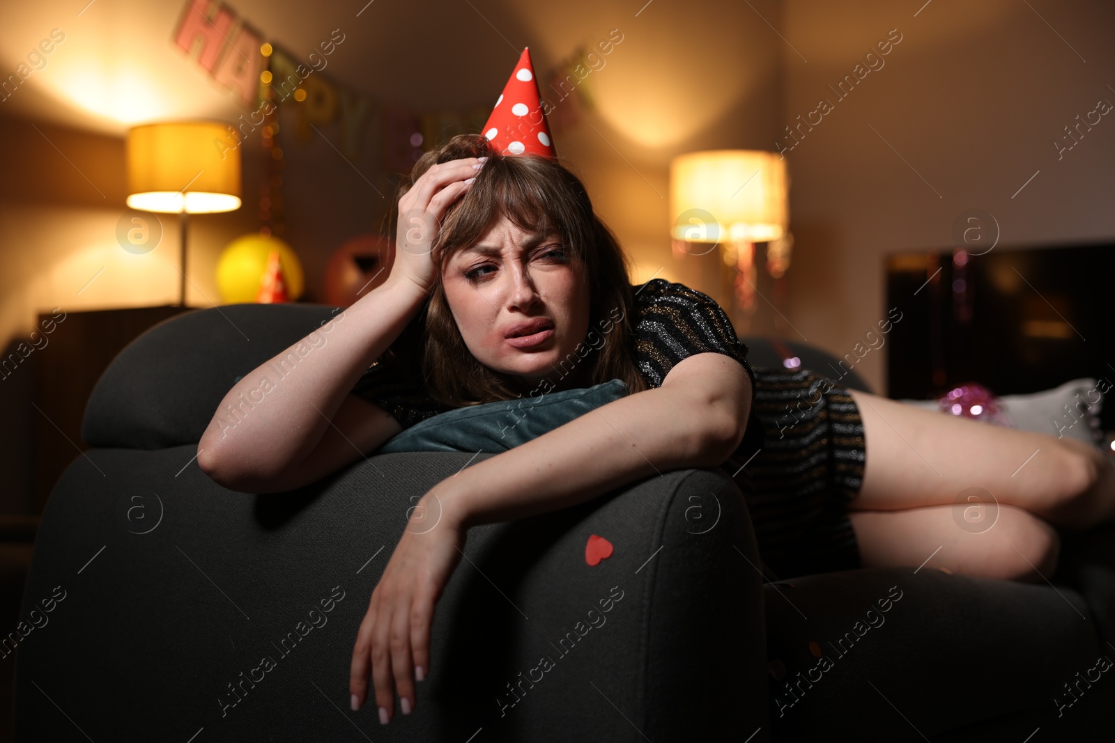 Photo of Woman suffering from hangover on sofa in messy room after party