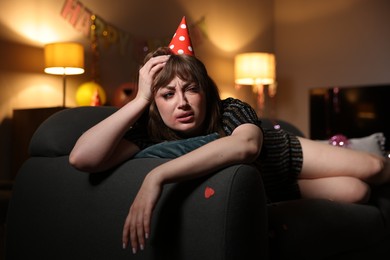 Photo of Woman suffering from hangover on sofa in messy room after party