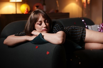 Photo of Woman suffering from hangover on sofa in messy room after party