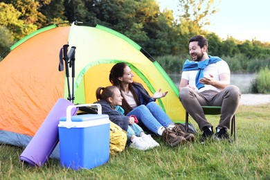 Photo of Happy family spending time together with camping tent and tourist equipment on green grass outdoors