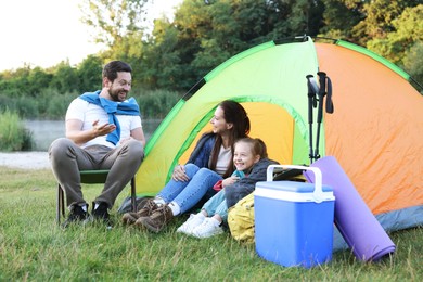 Photo of Happy family spending time together with camping tent and tourist equipment on green grass outdoors
