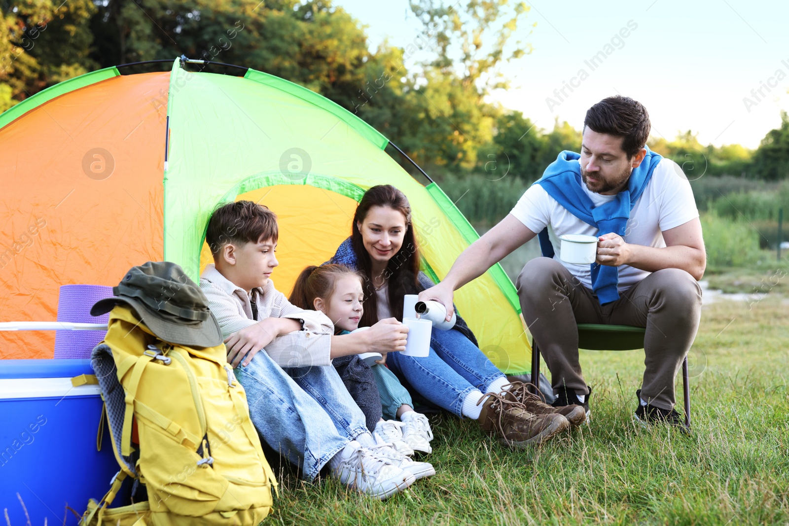 Family spending time together with camping tent, tourist equipment and mugs of hot drink outdoors Photo of Family spending time together with camping tent, tourist equipment and mugs of hot drink outdoors