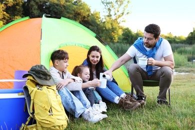 Photo of Family spending time together with camping tent, tourist equipment and mugs of hot drink outdoors