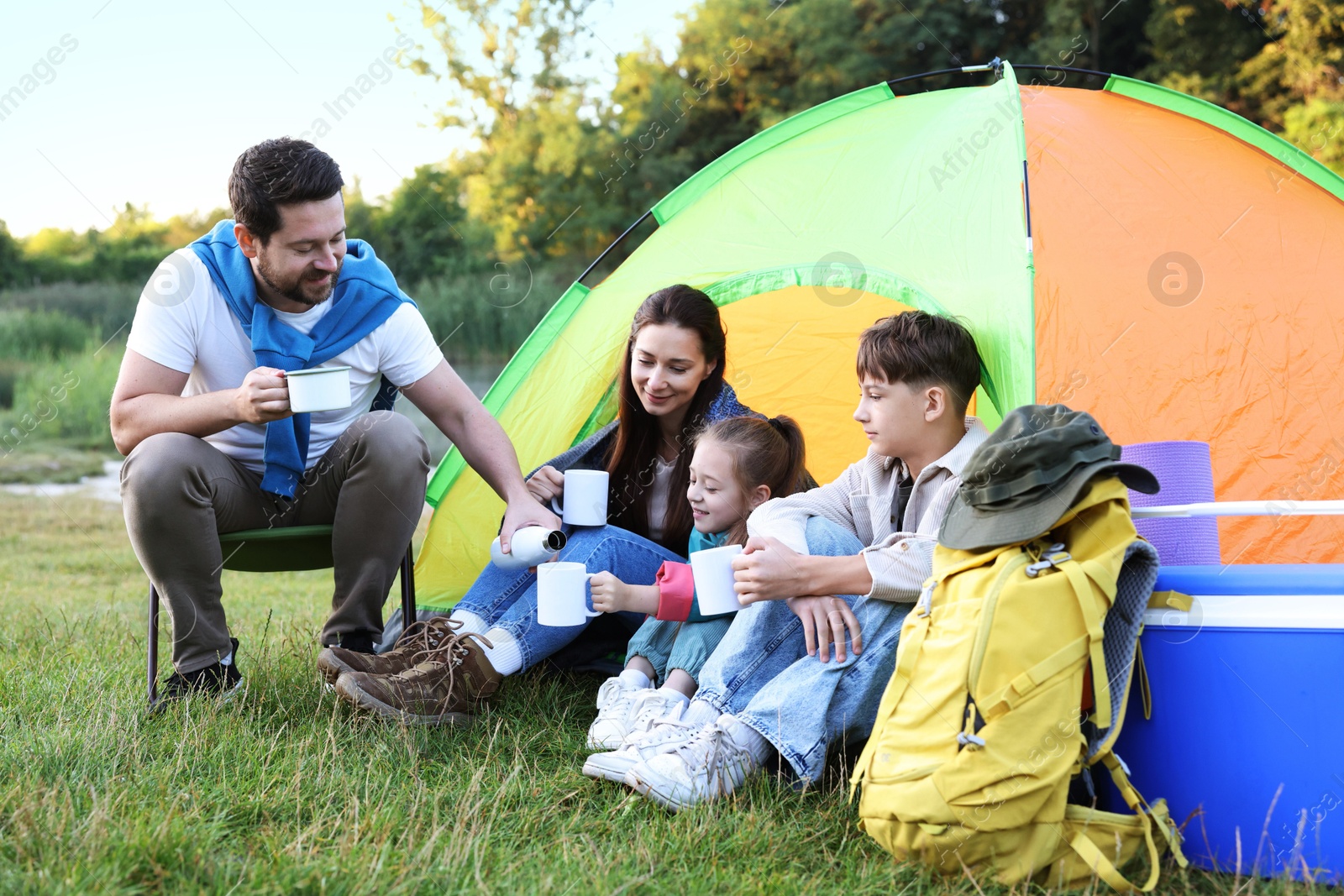 Photo of Family spending time together with camping tent, tourist equipment and mugs of hot drink outdoors