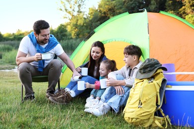 Photo of Family spending time together with camping tent, tourist equipment and mugs of hot drink outdoors
