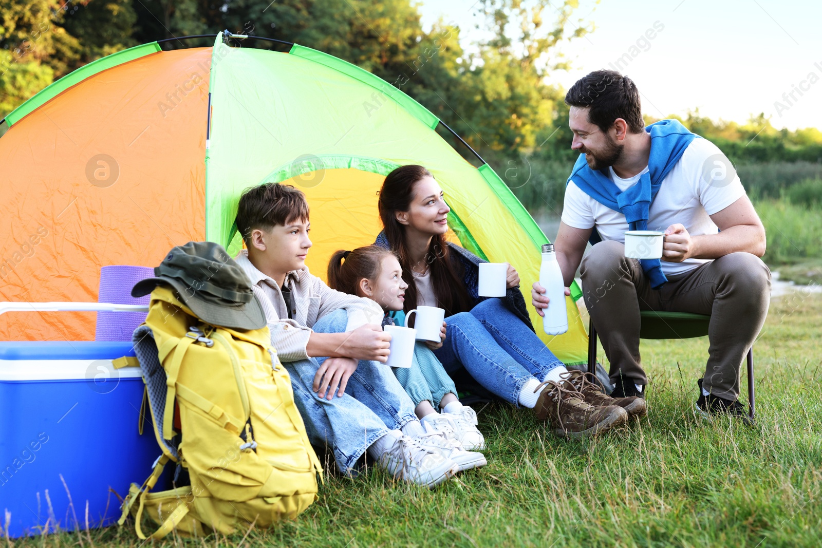 Happy family spending time together with camping tent, tourist equipment and mugs of hot drink outdoors Photo of Happy family spending time together with camping tent, tourist equipment and mugs of hot drink outdoors