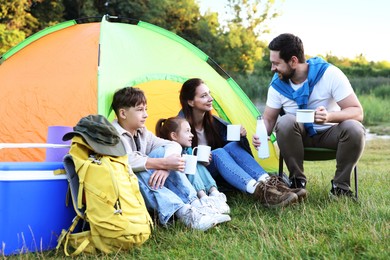 Photo of Happy family spending time together with camping tent, tourist equipment and mugs of hot drink outdoors