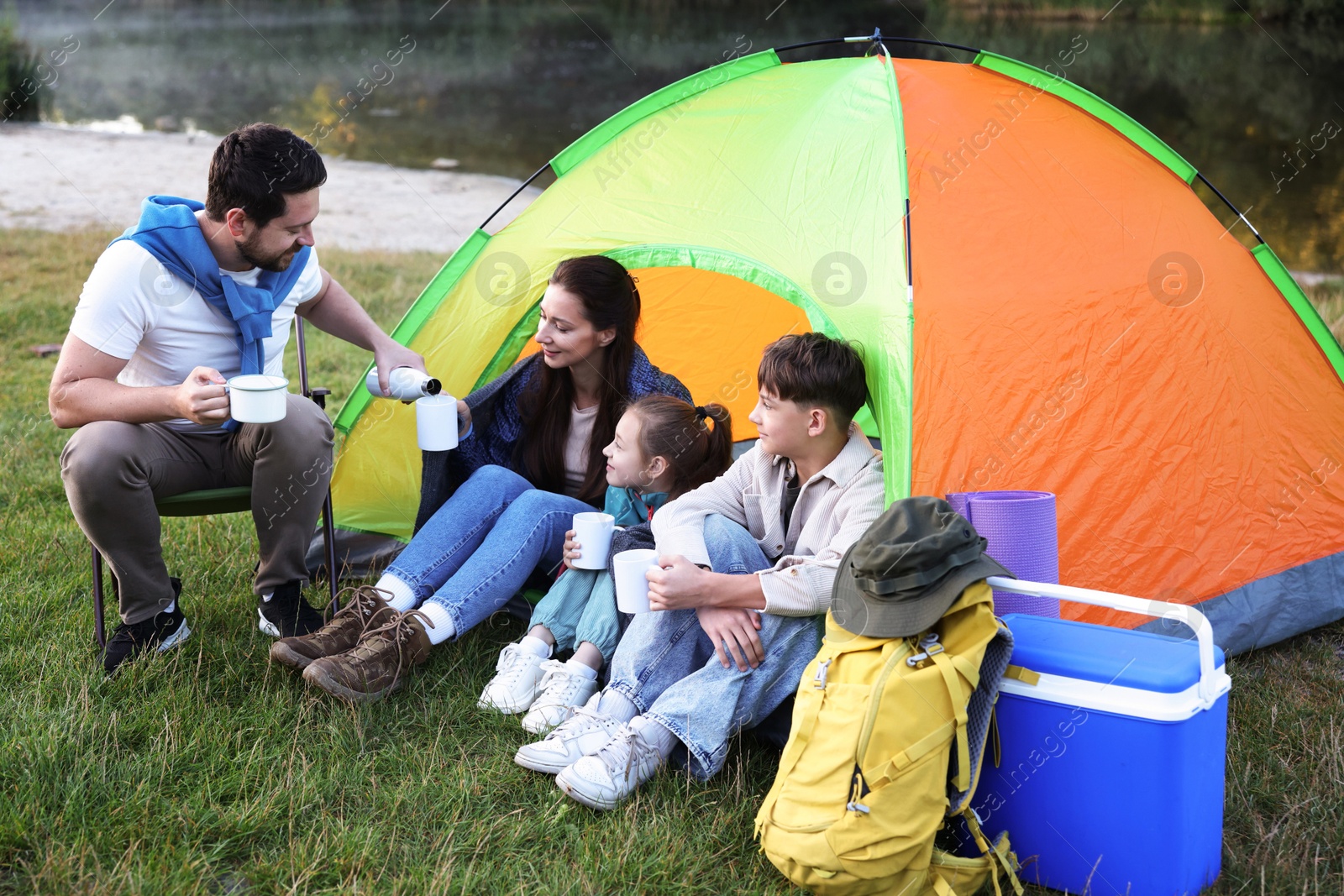 Happy family spending time together with camping tent, tourist equipment and mugs of hot drink outdoors Photo of Happy family spending time together with camping tent, tourist equipment and mugs of hot drink outdoors