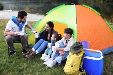 Photo of Happy family spending time together with camping tent, tourist equipment and mugs of hot drink outdoors