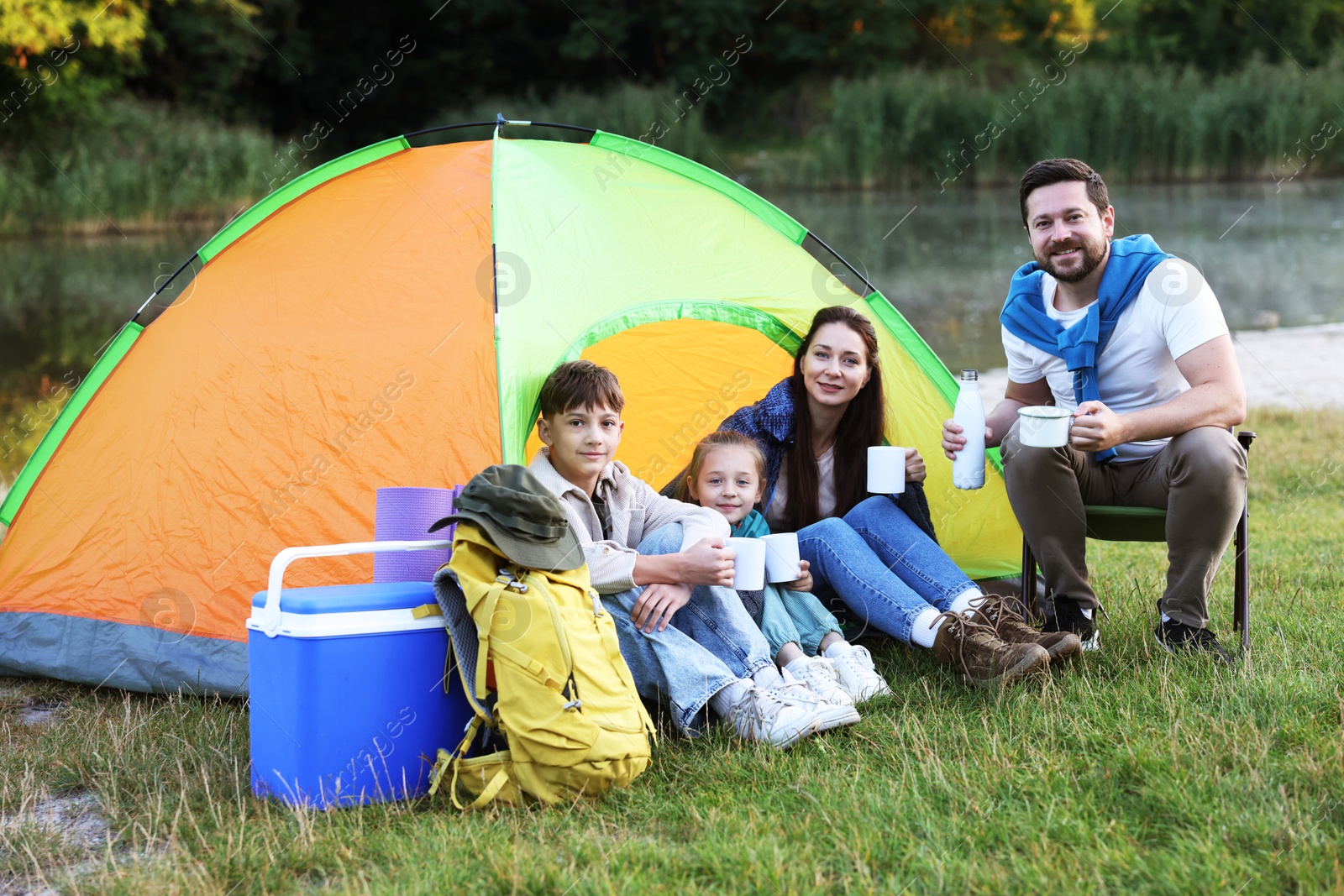 Photo of Happy family spending time together with camping tent, tourist equipment and mugs of hot drink outdoors