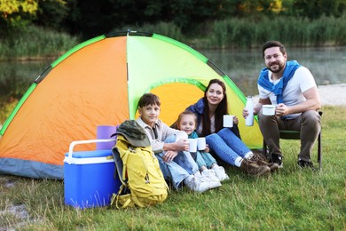 Photo of Happy family spending time together with camping tent, tourist equipment and mugs of hot drink outdoors