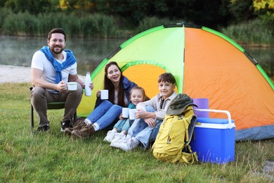 Photo of Happy family spending time together with camping tent, tourist equipment and mugs of hot drink outdoors