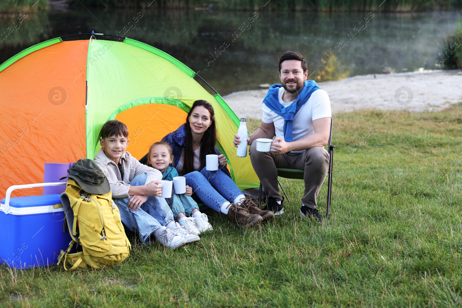 Happy family spending time together with camping tent, tourist equipment and mugs of hot drink outdoors Photo of Happy family spending time together with camping tent, tourist equipment and mugs of hot drink outdoors