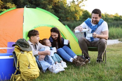 Photo of Happy family spending time together with camping tent, tourist equipment and mugs of hot drink outdoors