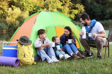 Photo of Happy family spending time together with camping tent, tourist equipment and mugs of hot drink outdoors
