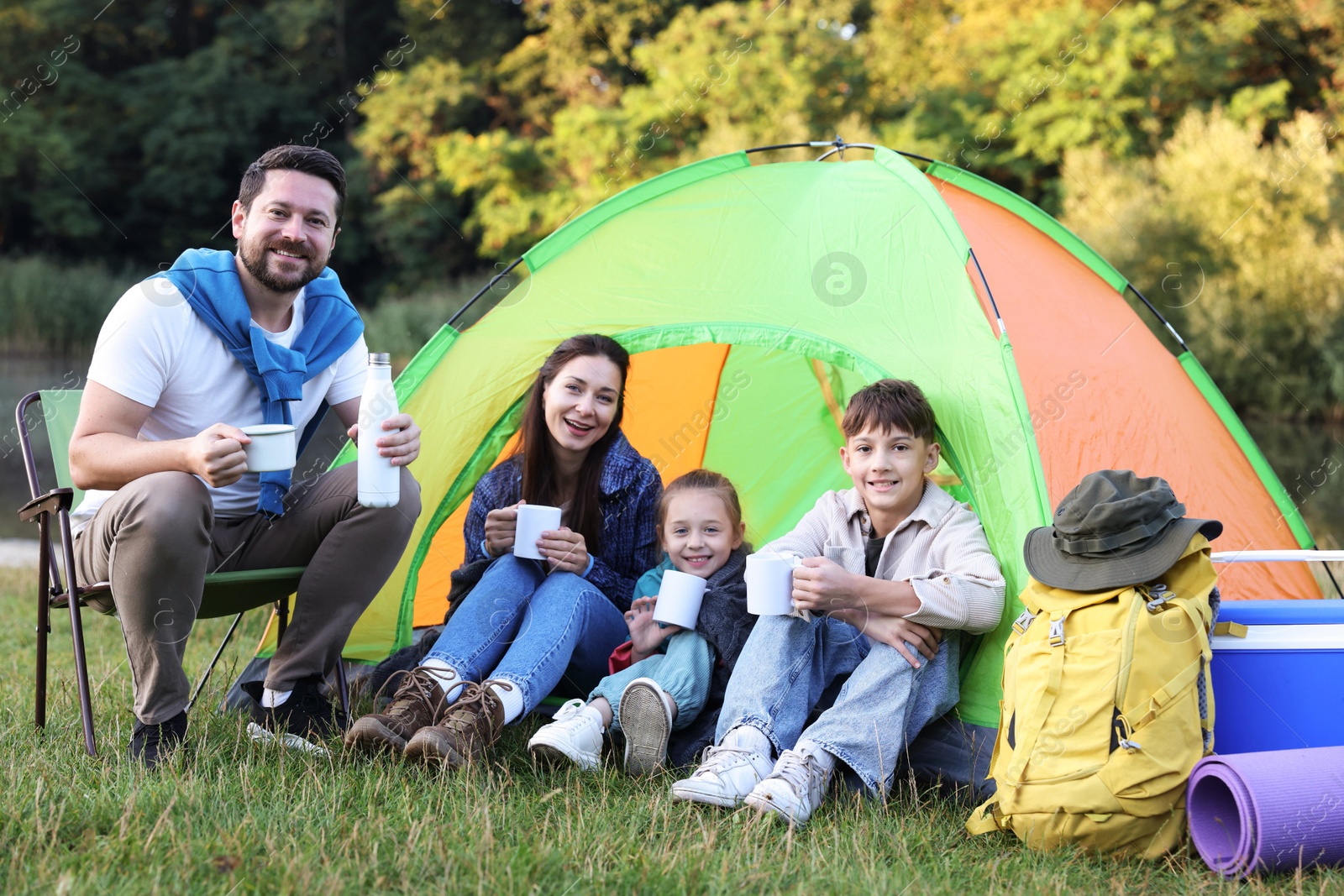 Happy family spending time together with camping tent, tourist equipment and mugs of hot drink outdoors Photo of Happy family spending time together with camping tent, tourist equipment and mugs of hot drink outdoors