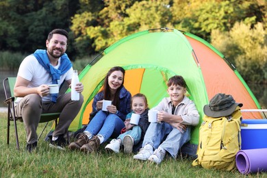 Photo of Happy family spending time together with camping tent, tourist equipment and mugs of hot drink outdoors