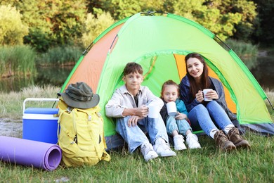 Photo of Happy family spending time together with camping tent, tourist equipment and mugs of hot drink outdoors