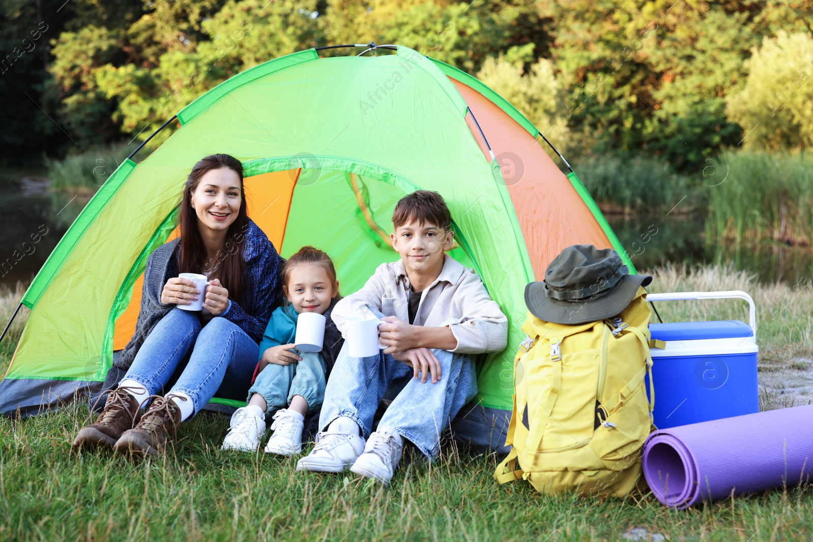 Happy family spending time together with camping tent, tourist equipment and mugs of hot drink outdoors Photo of Happy family spending time together with camping tent, tourist equipment and mugs of hot drink outdoors