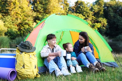 Photo of Family spending time together with camping tent, tourist equipment and mugs of hot drink outdoors