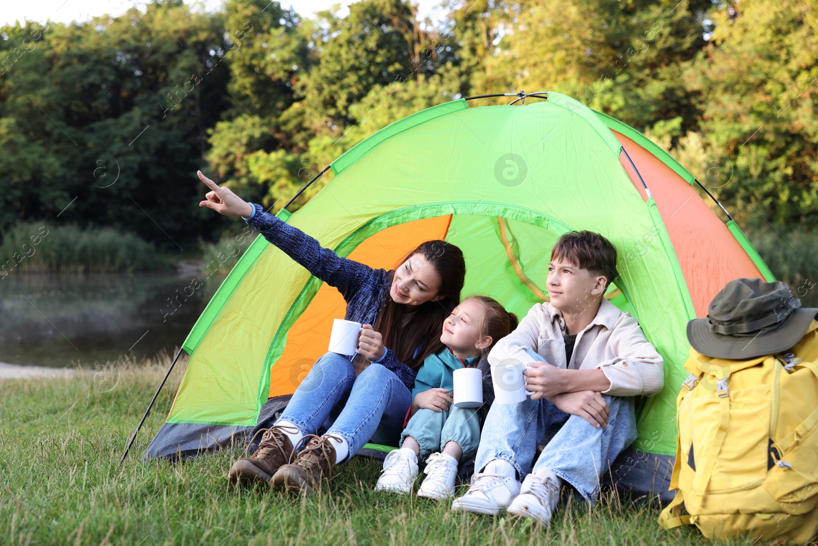 Happy family spending time together with camping tent, tourist equipment and mugs of hot drink outdoors Photo of Happy family spending time together with camping tent, tourist equipment and mugs of hot drink outdoors