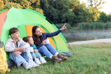 Photo of Happy family spending time together with camping tent and mugs of hot drink outdoors. Space for text