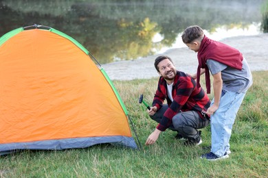 Photo of Happy father and son setting up camping tent near river outdoors
