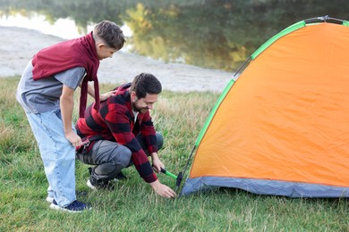 Photo of Happy father and son setting up camping tent near river outdoors