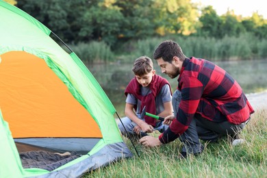 Photo of Father and son setting up camping tent near river outdoors