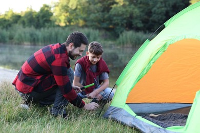Photo of Father and son setting up camping tent near river outdoors