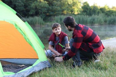 Photo of Father and son setting up camping tent near river outdoors
