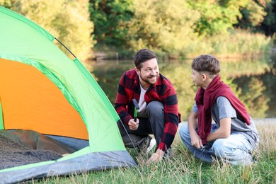 Photo of Happy father and son setting up camping tent near river outdoors