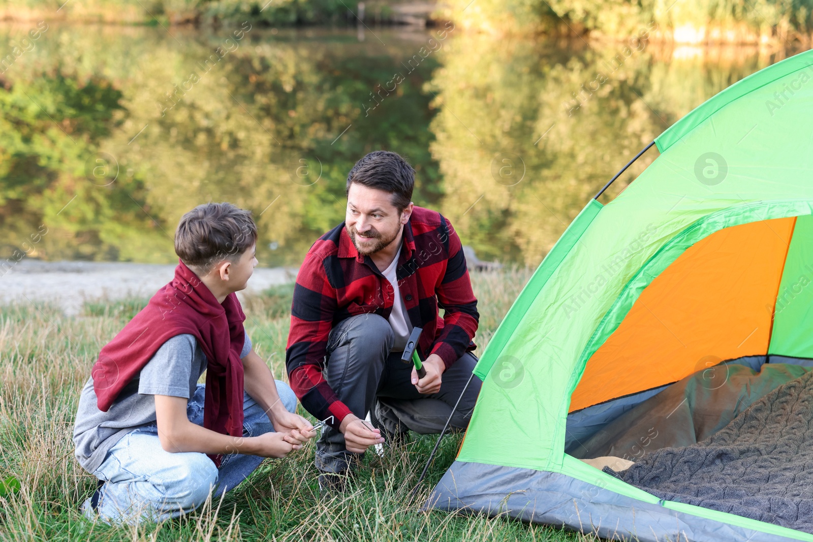 Photo of Happy father and son setting up camping tent near river outdoors