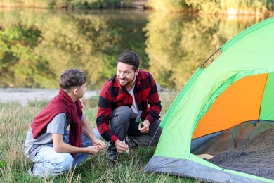 Photo of Happy father and son setting up camping tent near river outdoors
