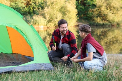 Photo of Happy father and son setting up camping tent near river outdoors