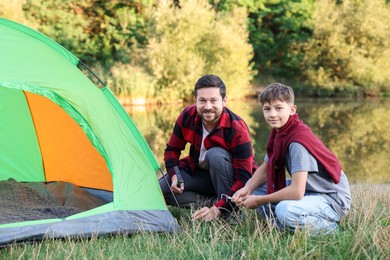 Photo of Happy father and son setting up camping tent near river outdoors