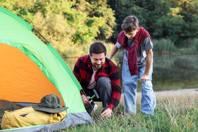 Photo of Father and son setting up camping tent near river outdoors