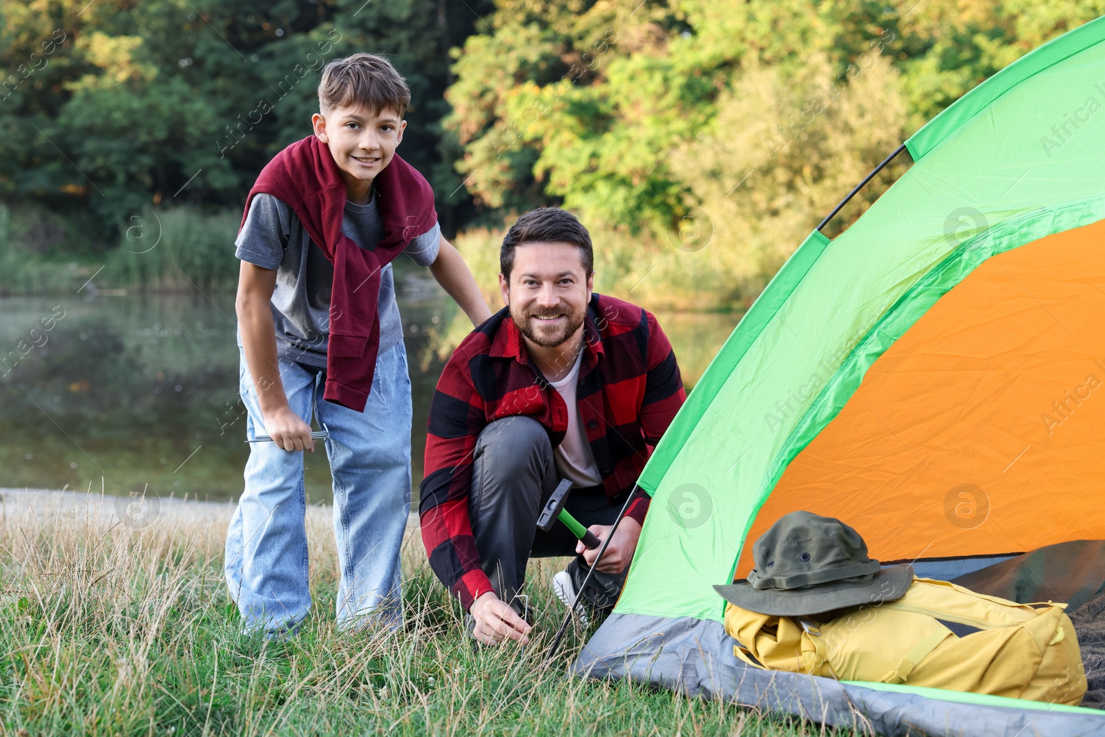 Happy father and son setting up camping tent near river outdoors Photo of Happy father and son setting up camping tent near river outdoors
