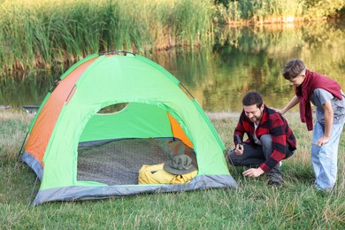 Photo of Father and son setting up camping tent near river outdoors