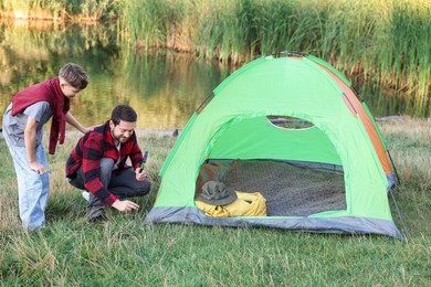 Photo of Father and son setting up camping tent near river outdoors