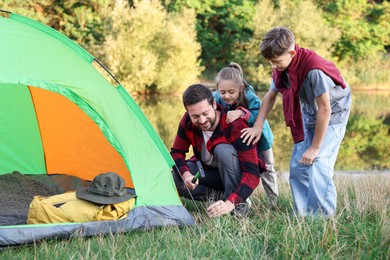 Photo of Happy father and his children setting up camping tent near river outdoors
