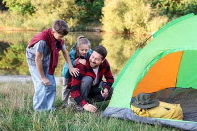 Photo of Happy father and his children setting up camping tent near river outdoors