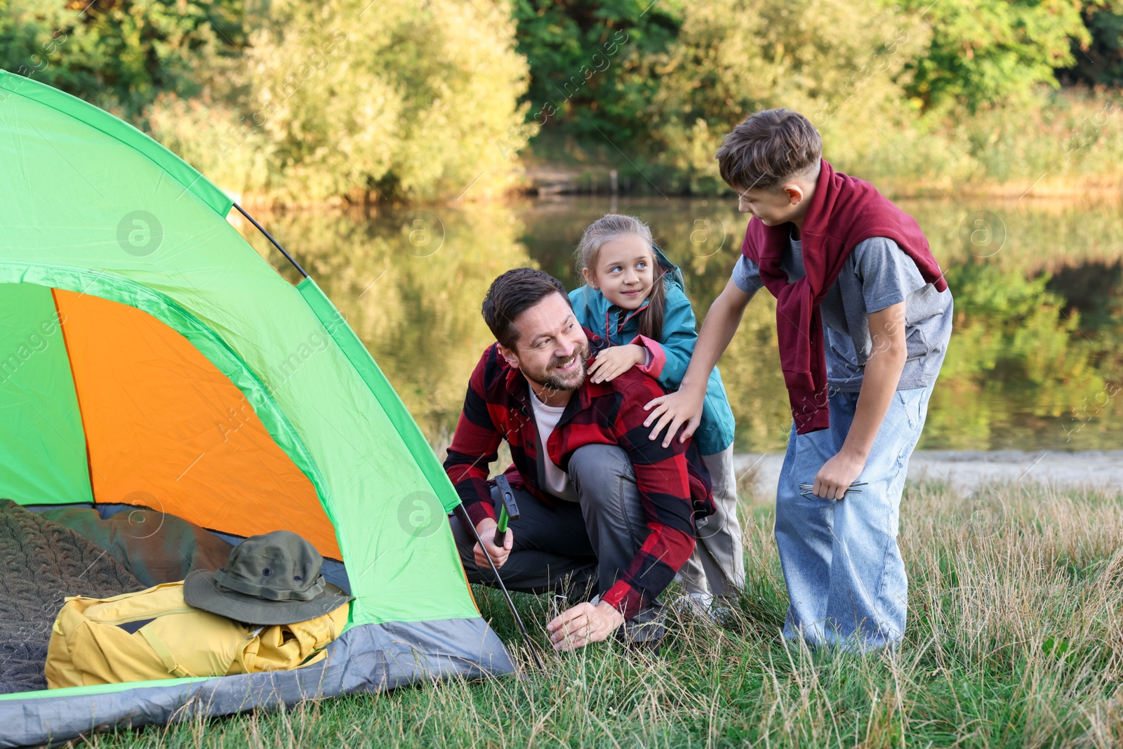 Photo of Happy father and his children setting up camping tent near river outdoors