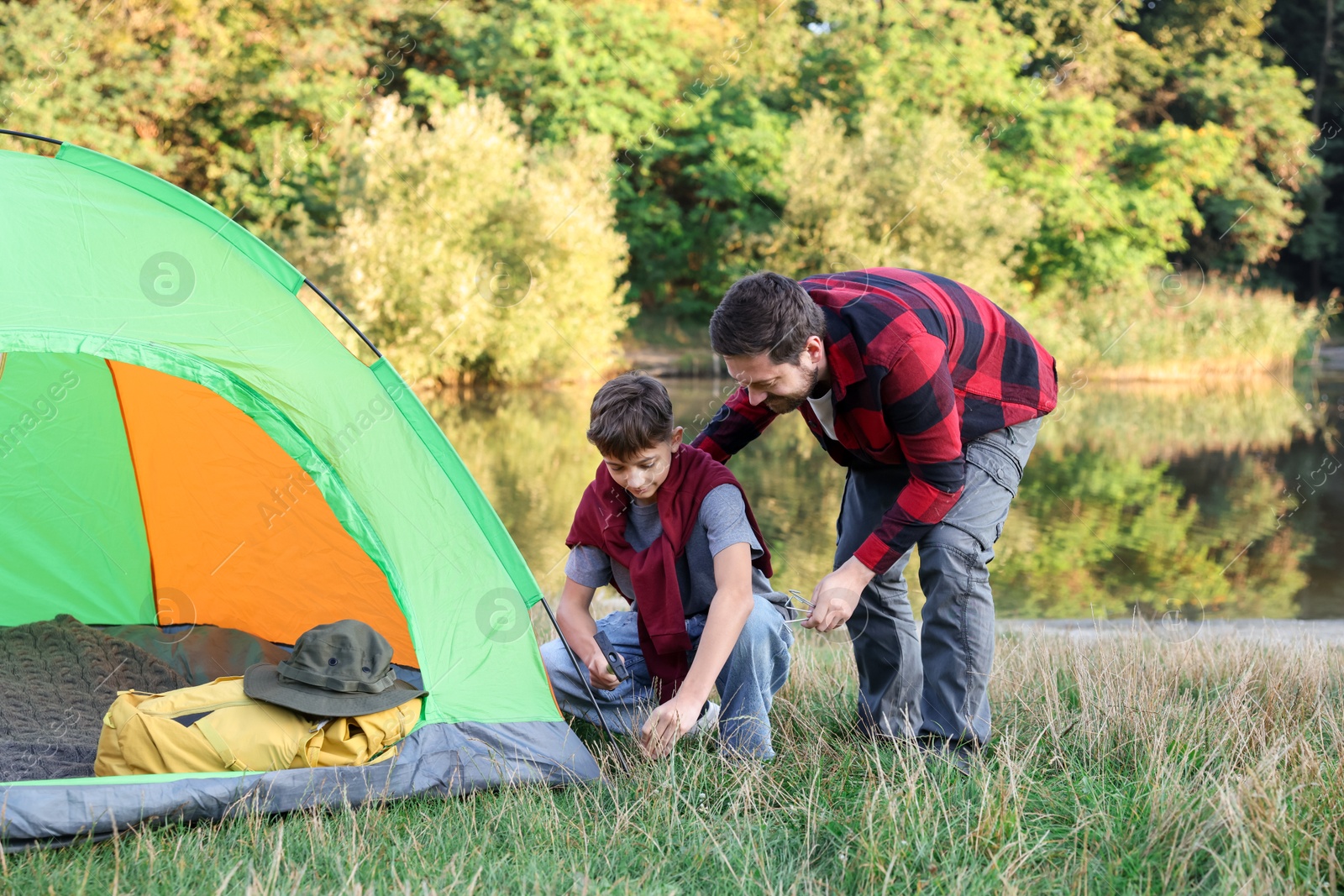 Photo of Father and son setting up camping tent near river outdoors