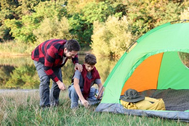Photo of Father and son setting up camping tent near river outdoors