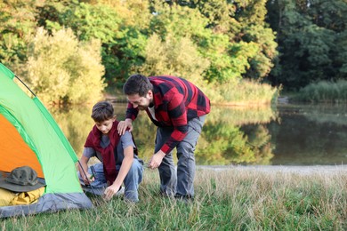 Photo of Father and son setting up camping tent near river outdoors. Space for text