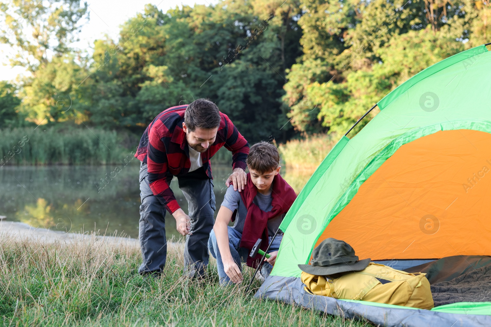 Photo of Father and son setting up camping tent near river outdoors