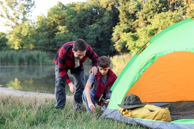 Photo of Father and son setting up camping tent near river outdoors